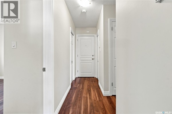Interior hallway with dark hardwood floors, white baseboards, and doors leading to rooms. - 22 2157 Rae Street, Regina
