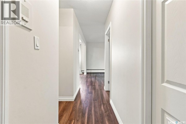 View down a long hallway with light gray walls, dark wood floors, and white trim. - 22 2157 Rae Street, Regina