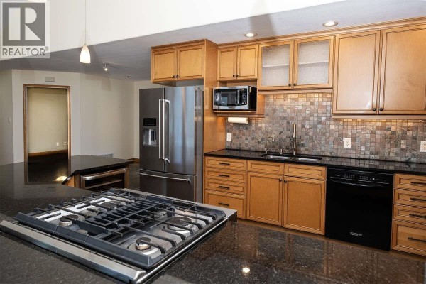 Close-up of kitchen with gas cooktop, stainless steel fridge, and wooden cabinetry - 22 4622 Sinclair Bay Road, Garden Bay