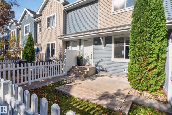 Concrete patio and grass area in front of a light blue townhouse with white picket fence. - #22 8304 11 Av Sw, Edmonton