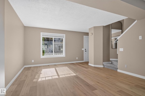 Living room with beige walls, light wood laminate flooring, and carpeted stairs. - #22 8304 11 Av Sw, Edmonton