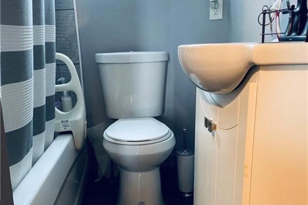 A white bathtub, toilet, and pedestal sink in a bathroom with a grey striped shower curtain. - 22 Alice Street, Hamilton