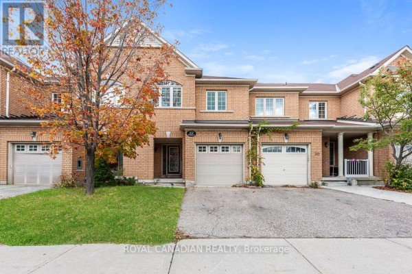 Brick townhouse exterior with a paved driveway and green lawn in daylight. - 22 Bay Breeze Drive, Brampton