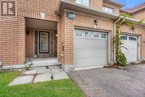 Front door and garage of a brick townhouse with a concrete walkway. - 22 Bay Breeze Drive, Brampton