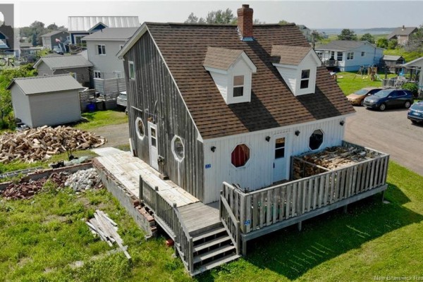 Back view of the house with a wooden deck and stacked firewood. - 22 Beach Street, Pointe Du Chene