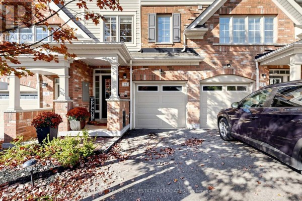 Driveway and entrance to a townhouse with a garage door and decorative pillars. - 22 Benjamin Way, Whitby