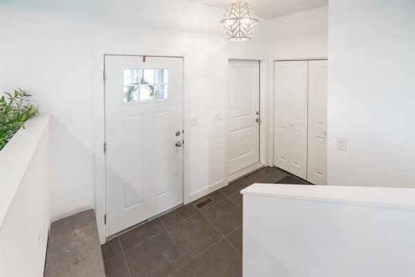 View from the entryway towards the living and dining areas, featuring a staircase and white partition walls. - 22 Bramblewood Street, Kleefeld