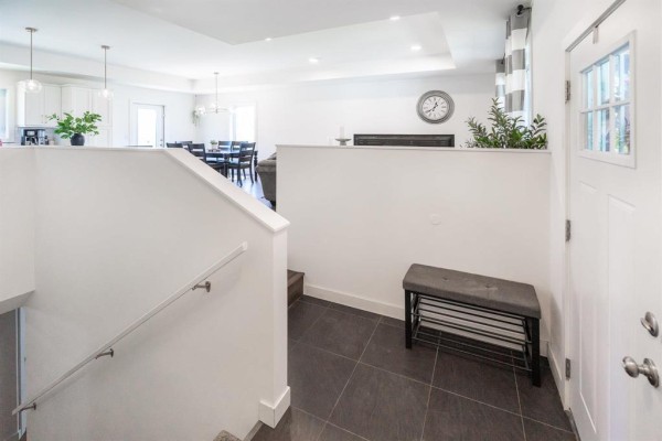 View of the living room from the top of the stairs, showing grey sofas, a fireplace, and windows with striped curtains. - 22 Bramblewood Street, Kleefeld