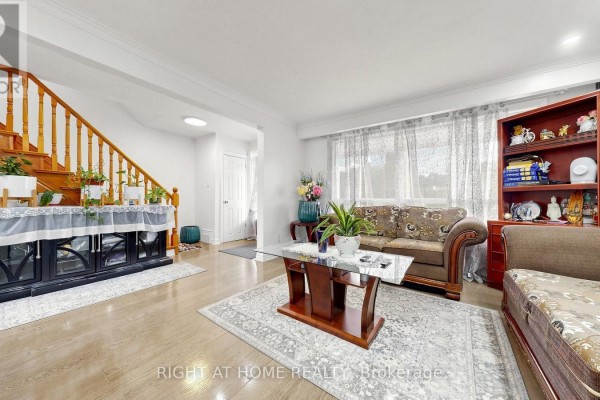 Living room with hardwood floors, sofa, armchair, coffee table, and staircase. - 22 Brigham Court, Toronto