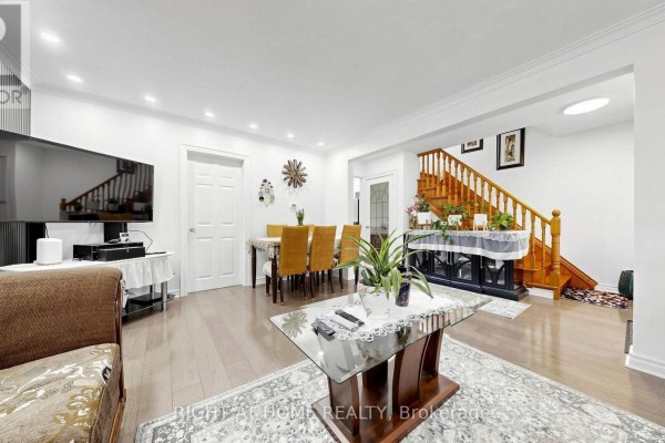 Living and dining area with hardwood floors, sofa, dining set, and staircase. - 22 Brigham Court, Toronto