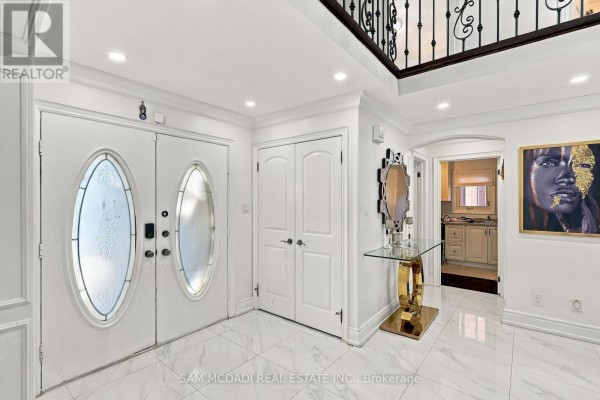 Bright foyer with white marble tile floors, double white doors, and a gold console table. - 22 Butlers Court, Brampton
