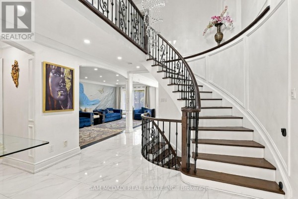 Spacious foyer with white marble tile, a grand curved staircase with dark wood banister, and chandelier. - 22 Butlers Court, Brampton