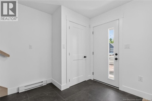 Interior entryway with white walls, a closed white door, dark grey tiled floor, and a white front door. - 22 Cedric Court, Dieppe
