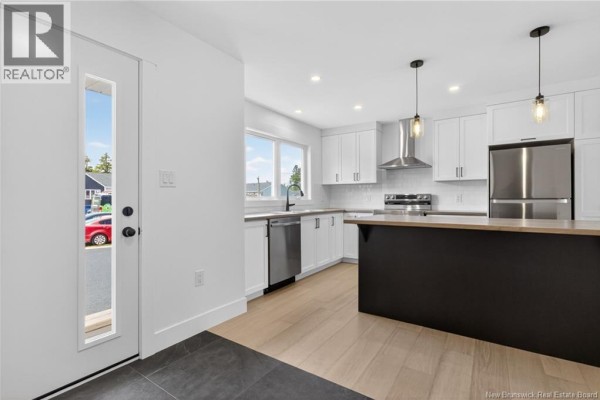 Modern kitchen with white cabinets, stainless steel appliances, a black island with a wood countertop, and light wood floors. - 22 Cedric Court, Dieppe