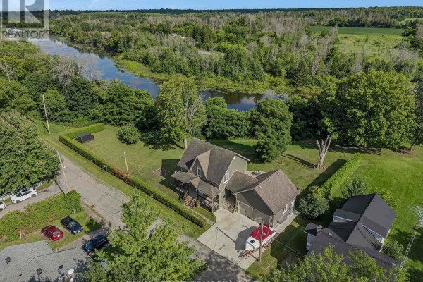 Aerial view of a residential property with a house, attached garage, boat, and surrounding trees and water. - 22 Centre Street, North Grenville