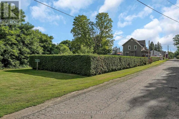 View of the side of a house from a street, partially obscured by a tall, well-maintained hedge. - 22 Centre Street, North Grenville