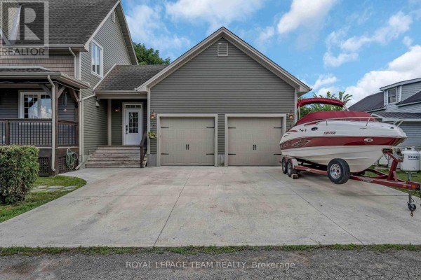 Front view of an attached two-car garage with two beige doors and a boat on a trailer parked on the concrete driveway. - 22 Centre Street, North Grenville