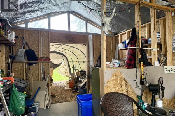 Interior of a storage shed with exposed wood framing, shelves, tools, and a view into a greenhouse. - 22 Chamberlain Street, Amherst
