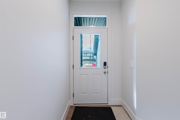 Front entrance with a white door, glass transom, and wood-look flooring. A black doormat is visible. - 22 Clichy Cl, St  Albert