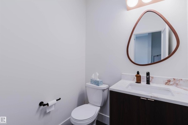 Powder room with a white toilet, marble countertop vanity with dark wood cabinets, and a triangular mirror. - 22 Clichy Cl, St  Albert