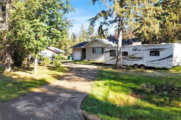 Side view of a house with a garage, an adjacent RV, and a wooded setting. - 22 College Park Close, Red Deer