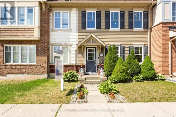 Front entrance of a beige townhouse with a black door, flanked by manicured shrubs. - 22 Crossbill Road, Brampton