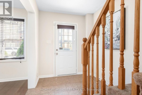 Interior foyer with a white door, tiled floor, and light wood staircase railing. - 22 Crossbill Road, Brampton