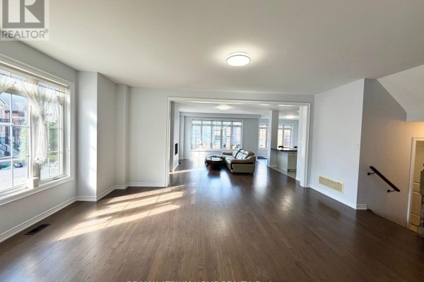 Open-concept living and dining area with dark hardwood floors, large windows, and light gray walls. - 22 Duggan Street, Aurora