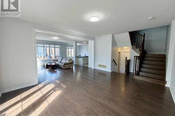 Interior view of a living area with dark hardwood floors, a staircase, and an opening to another room. - 22 Duggan Street, Aurora