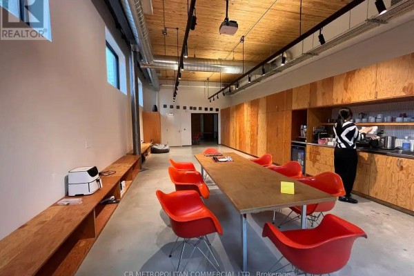 Office common area with a long wooden table, orange chairs, and light wood cabinetry. - 22 Geary Avenue, Toronto