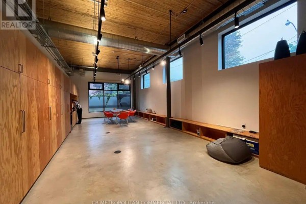 Spacious open-concept office with concrete floors, wood paneling, and large windows. - 22 Geary Avenue, Toronto