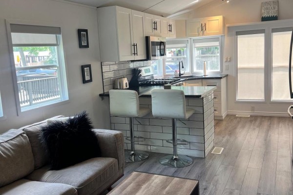 Living area facing a kitchen island with two white bar stools and white subway tile. - 22 Hickory Lane, Port Colborne