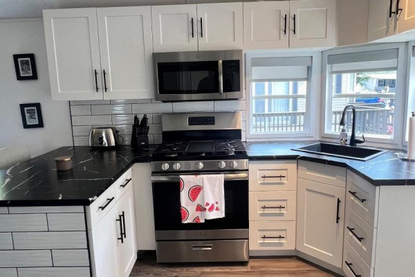 Close-up of a kitchen with white cabinets, black countertops, and stainless steel appliances. - 22 Hickory Lane, Port Colborne