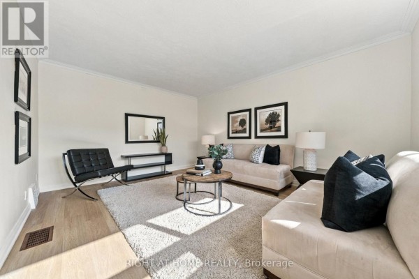 Living room with light-colored sofas, black armchair, coffee table, and hardwood floors. - 22 Katherine Road, Toronto