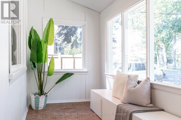 Sunroom with large windows, white built-in seating, and a large potted plant. - 22 Long Branch Avenue, Toronto