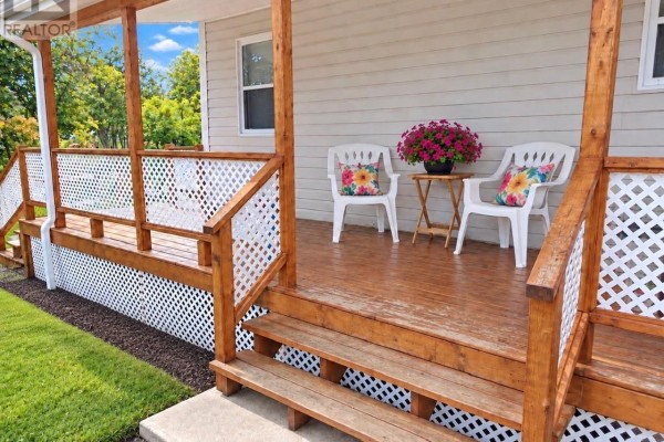 Side view of a wooden porch with white lattice railings, two chairs, and flower pots. - 22 Main Street, Hare Bay