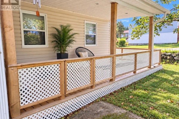 Covered porch with wooden posts, white lattice railing, and an outdoor chair. - 22 Main Street, Hare Bay
