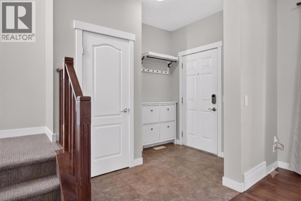 Interior view of the entrance foyer with tiled floor, white doors, and a wooden staircase with carpet runner. - 22 Panora Road Nw, Calgary