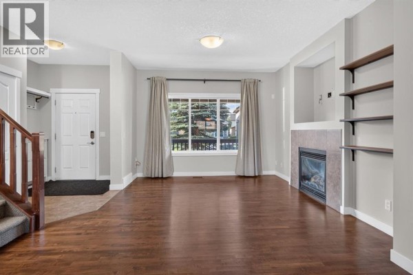 Living room with dark hardwood floors, a fireplace with tiled surround, and large window with beige curtains. - 22 Panora Road Nw, Calgary
