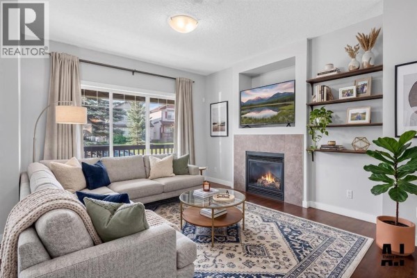 Living room with a sectional sofa, coffee table, fireplace, and built-in shelving units displaying decor. - 22 Panora Road Nw, Calgary