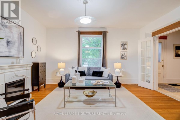 Living room featuring a white fireplace, gray sofa, glass coffee table, and hardwood floors. - 22 Peel Avenue, Brampton