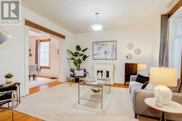 Living room with a fireplace, gray sofa, glass coffee table, and views into the dining room. - 22 Peel Avenue, Brampton