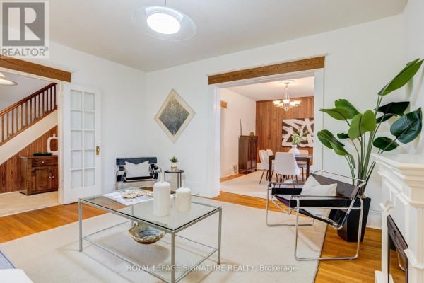 Living room with hardwood floors, fireplace, glass coffee table, and a view into the dining area. - 22 Peel Avenue, Brampton