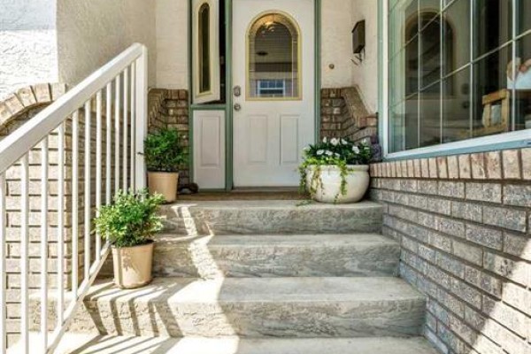 Close-up of front entry stairs with potted plants and a white door with arched glass. - 22 Penland Way Ne, Medicine Hat