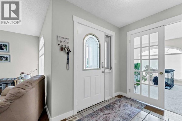 Interior foyer with a white front door, tiled floor, rug, and glass-paneled doors. - 22 Penland Way Ne, Medicine Hat
