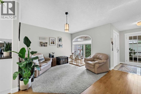 Living room with tan sofas, textured rug, large arched window, and wood flooring. - 22 Penland Way Ne, Medicine Hat