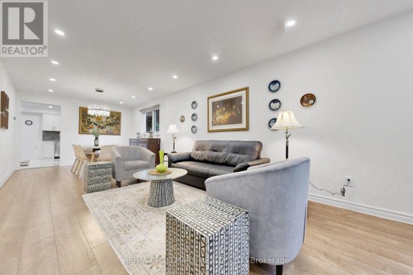 Living room with a dark sofa, light grey armchairs, and wood-look flooring. - 22 Pining Road, Markham