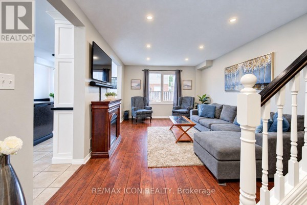 Living room with a grey sectional sofa, fireplace, hardwood floors, and a staircase. - 22 Poffenroth Path, Woolwich