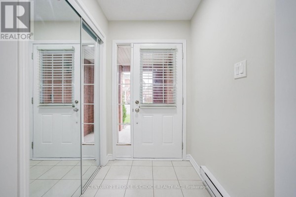 Interior foyer with white tile floors, white walls, and a mirrored closet door. - 22 Quillberry Close, Brampton