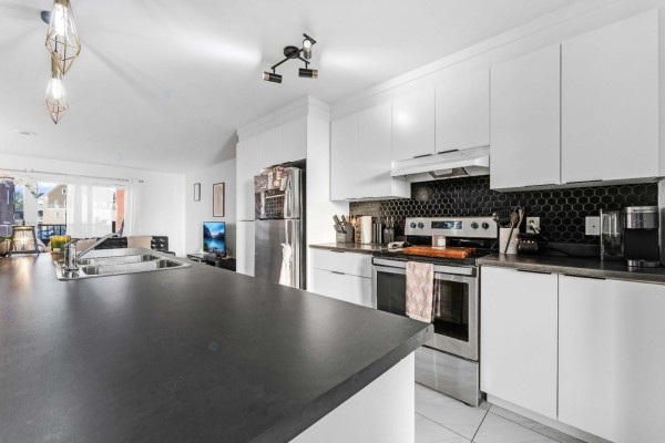 Open concept kitchen and living area with white cabinets, black backsplash, stainless steel appliances, and island. - 22 Rue St-pétersbourg, Gatineau